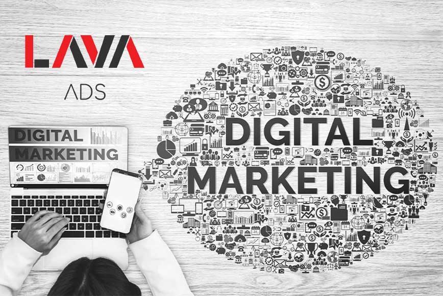 Digitalni marketing ispisan u oblačiću ikonica na radnom stolu i osoba koja sedi za računarom dok koristi mobilni telefon iz ptičije perspektive.